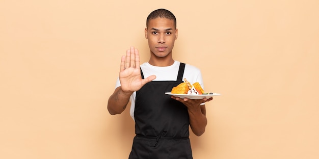 Young black man looking serious, stern, displeased and angry showing open palm making stop gesture