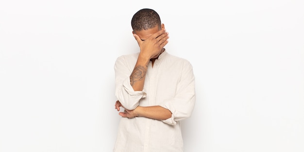 young black man looking stressed, ashamed or upset, with a headache, covering face with hand