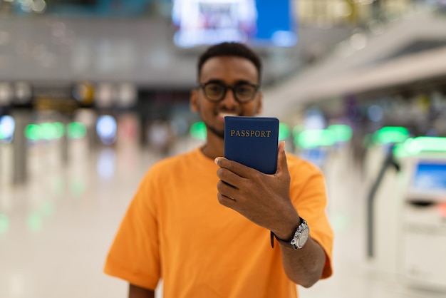 Young black man ready to travel at airport terminal and showing passport