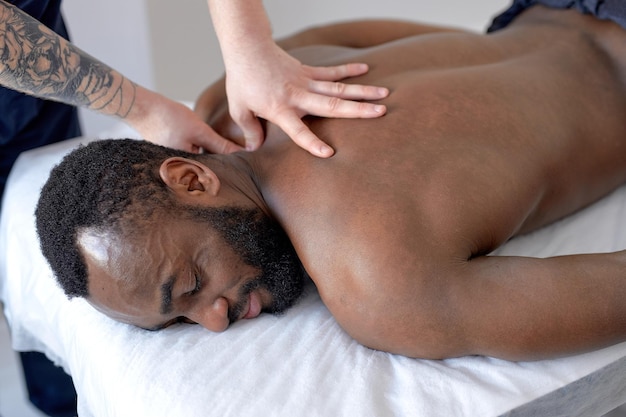 Young black man receiving back massage in spa wellness center professional masseur