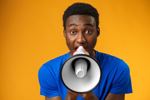 Young black man shouting in megaphone on yellow background