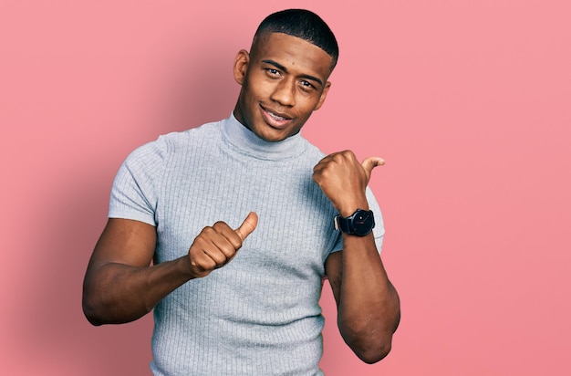 Young black man wearing casual t shirt pointing to the back behind with hand and thumbs up, smiling confident