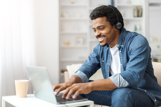 Young black man with headphones working on laptop indoors