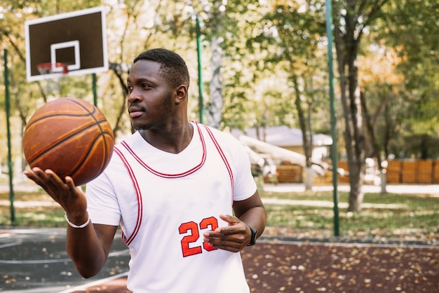 Young black smiling man playing basketball on the court at sunrise, morning sports. Outdoor portrait.