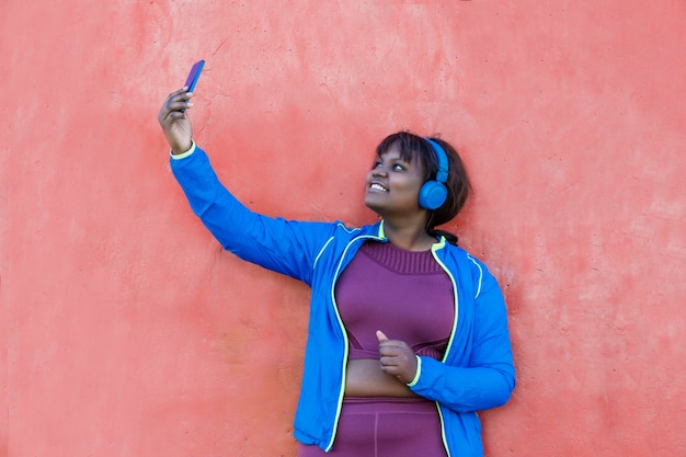 Young black woman against a colorful wall looking at her cell phone taking a selfie