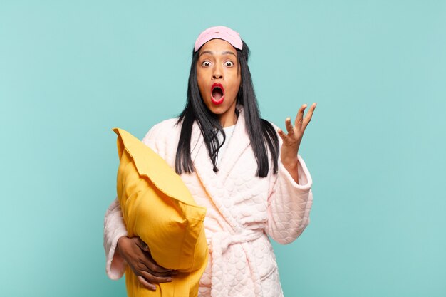 Young black woman feeling extremely shocked and surprised, anxious and panicking, with a stressed and horrified look. pajamas concept