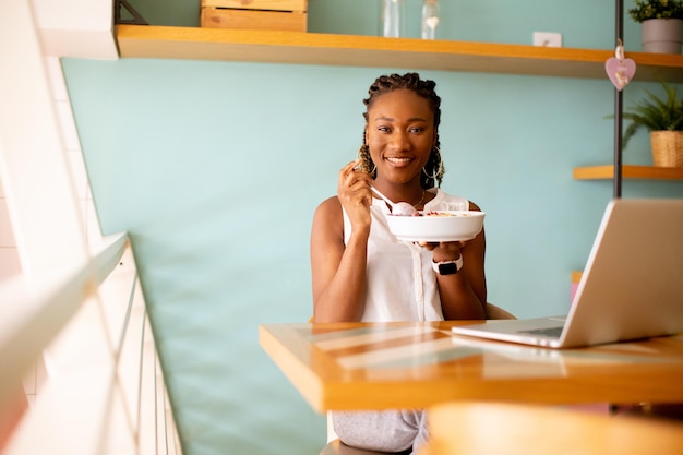 Young black woman having a healthy breakfast while working on laptop in the cafe