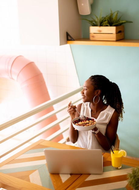 Young black woman having a healthy breakfast while working on laptop in the cafe