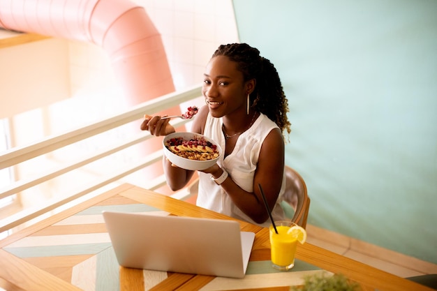 Young black woman having a healthy breakfast while working on laptop in the cafe