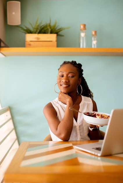 Young black woman having a healthy breakfast while working on laptop in the cafe