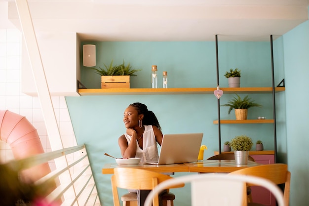 Young black woman having a healthy breakfast while working on laptop in the cafe