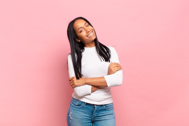 Young black woman laughing happily with arms crossed, with a relaxed, positive and satisfied pose