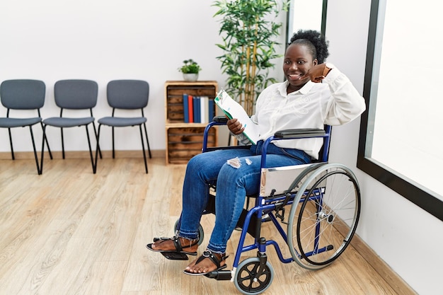 Young black woman sitting on wheelchair at waiting room smiling cheerful showing and pointing with fingers teeth and mouth dental health concept