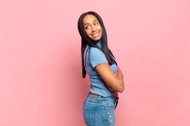 Young black woman smiling gleefully, feeling happy, satisfied and relaxed, with crossed arms and looking to the side