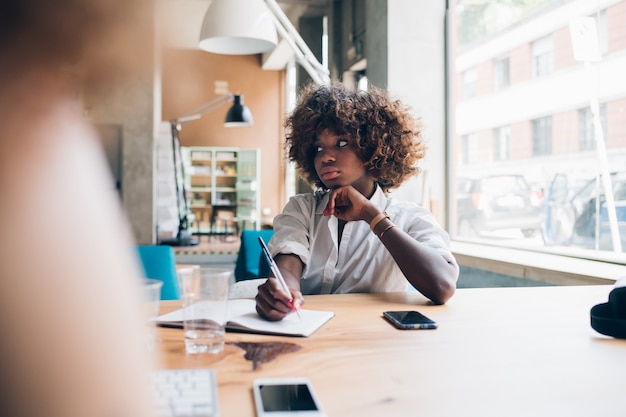 Young black woman writing during meeting 