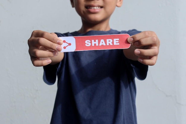 Young blogger boy showing printed paper with Share text, asking people to share his video. Blogging,