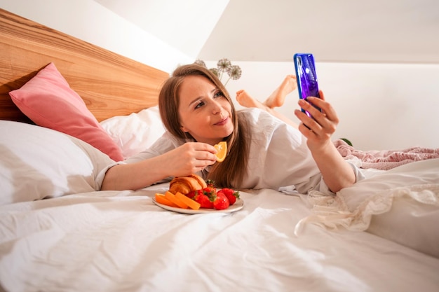 Young blogger creating content taking selfie during breakfast in bed