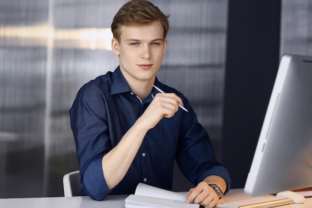 Young blond businessman thinking about strategy at his working place with computer. Startup business means working hard and out of time for success achievement.