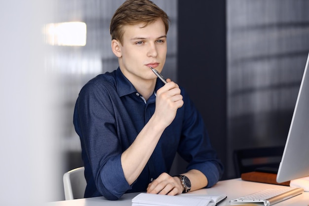 Young blond businessman thinking about strategy at his working place with computer. Startup business means working hard and out of time for success achievement.