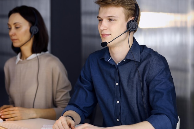 Young blond businessman using headset and computer at work. Startup business means working hard and out of time for success achievement.