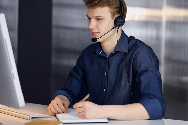 Young blond businessman using headset and computer at work. Startup business means working hard and out of time for success achievement.