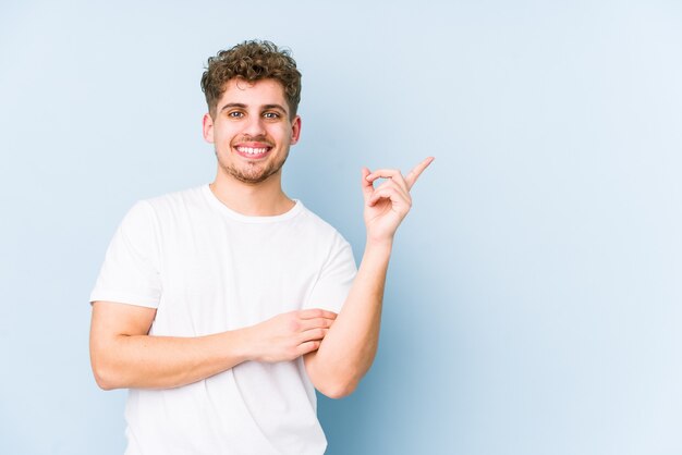 Young blond curly hair caucasian man isolated smiling cheerfully pointing with forefinger away.