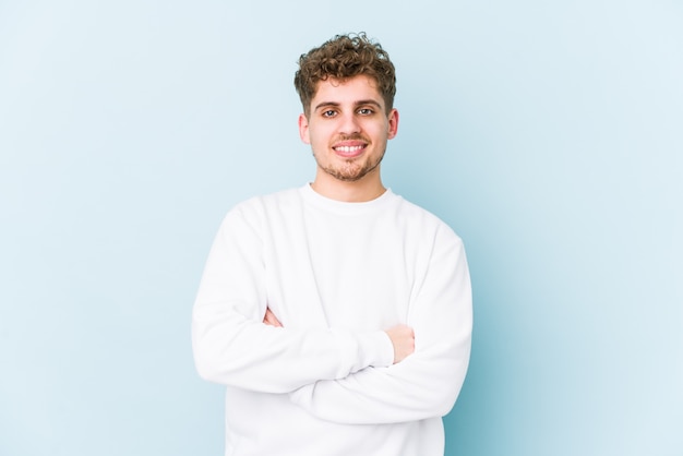 Young blond curly hair caucasian man isolated who feels confident, crossing arms with determination.