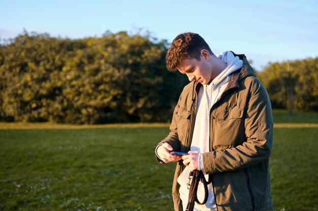 Young blond man looking with interest and strangeness at the screen of his mobile phone in a park