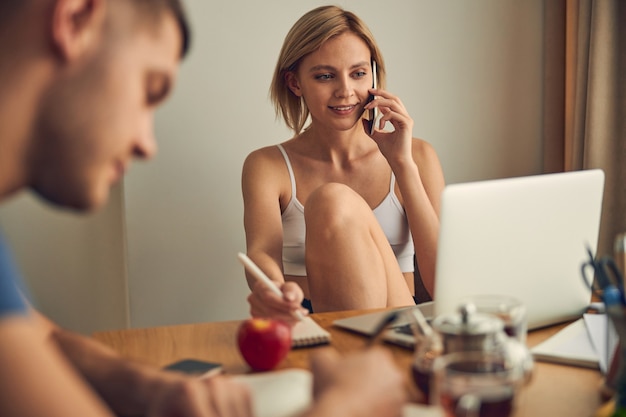 Young blond woman in casual clothes working on computer and calling while brunette man writing