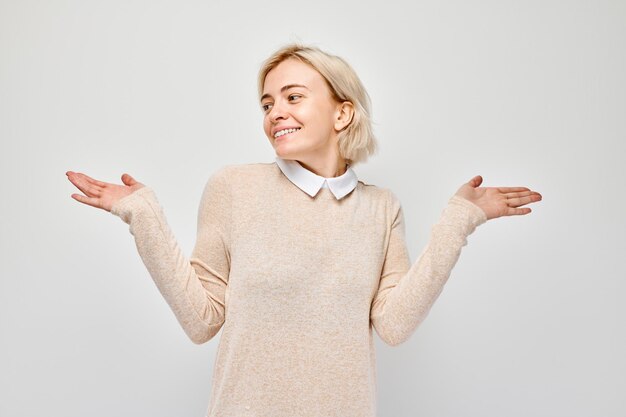 Young blond woman in casual holding something in hand demonstrating empty space for product or text isolated on white studio background