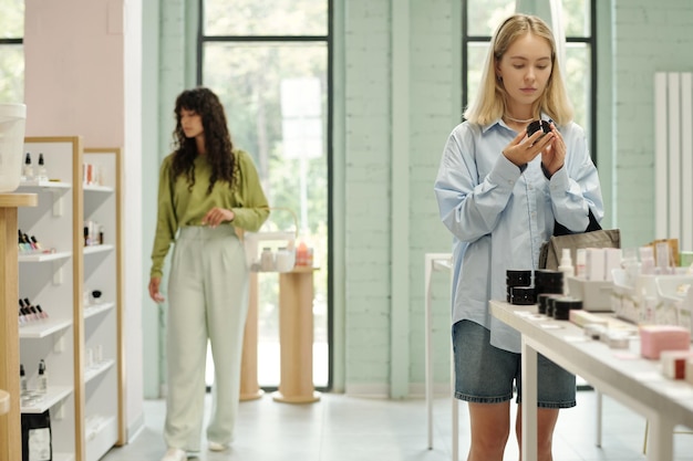 Young blond woman choosing compact powder while standing by display