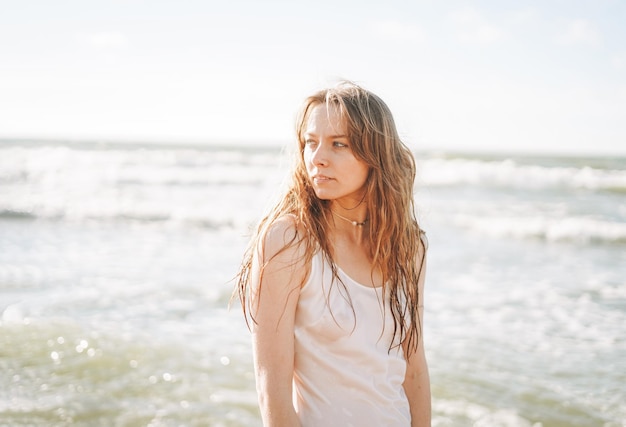 Young blonde beautiful woman with long hair in white dress enjoying life on sea beach