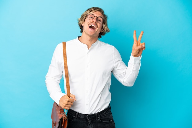 Young blonde businessman isolated on blue smiling and showing victory sign