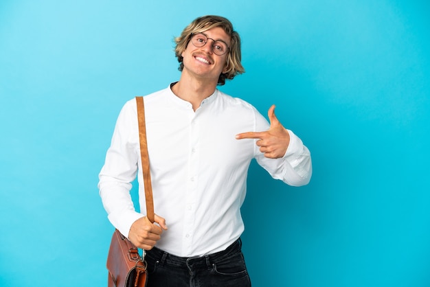 Young blonde businessman isolated on blue wall proud and self-satisfied