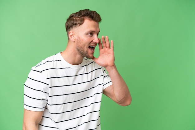 Photo young blonde caucasian man over isolated background shouting with mouth wide open to the side