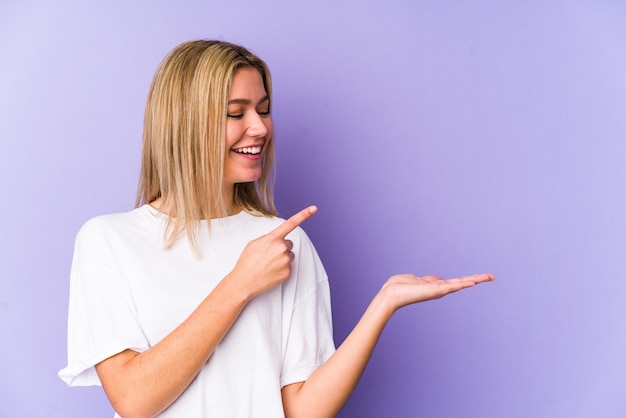 Young blonde caucasian woman isolated excited holding a copy space on palm.