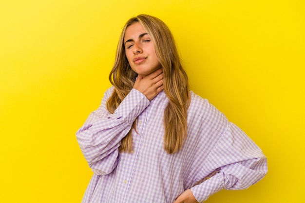 Young blonde caucasian woman isolated on yellow wall suffers pain in throat due a virus or infection.