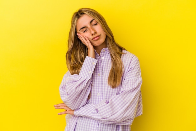 Young blonde caucasian woman isolated on yellow wall who is bored, fatigued and need a relax day