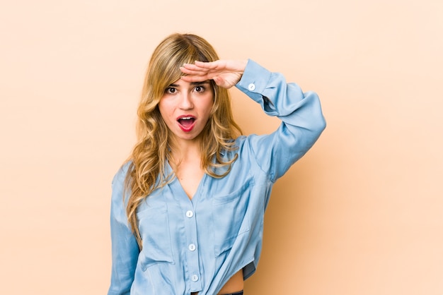 Young blonde caucasian woman looking far away keeping hand on forehead.