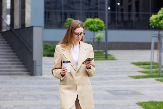 A young blonde girl against the backdrop of a business center office center On the go he reads the news from his smartphone