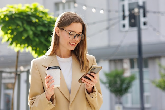 A young blonde girl against the backdrop of a business center office center Portrait of a successful startup Smartphone coffee casual suit