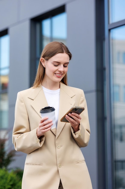 A young blonde girl against the backdrop of a business center office center Portrait of a successful startup Smartphone coffee casual suit