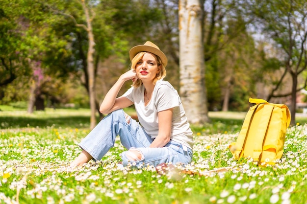 A young blonde girl in a hat enjoying spring in a park in the city vacations next to nature and next to daisies