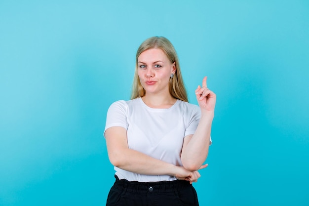 Young blonde girl is pointing up with forefinger on blue background