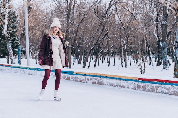 Young blonde girl skating in snowy winter park.