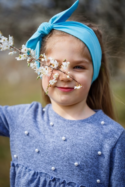 Young blonde girl standing in a blooming garden. Blooming cherry. Portrait of beautiful little girl. Close up of little model face. Sakura blooming, spring evening time