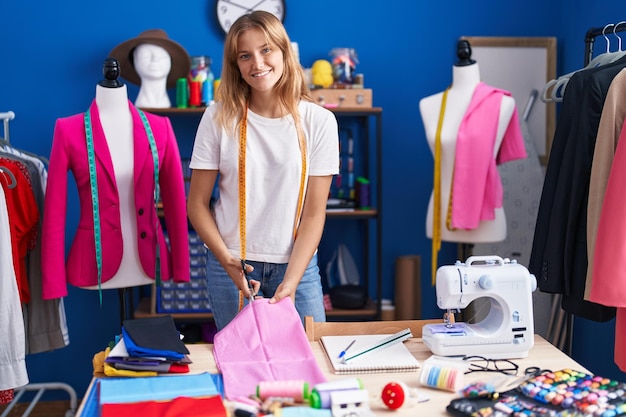 Young blonde girl tailor cutting cloth at sewing studio