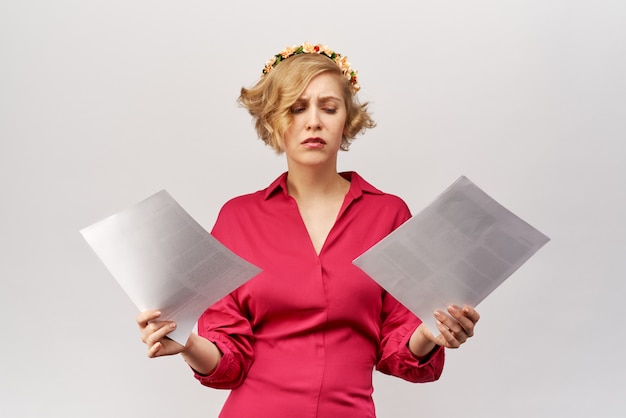 A young blonde girl with a lost view looks at the documents spreading her hands in front of her in confusion and misunderstanding.