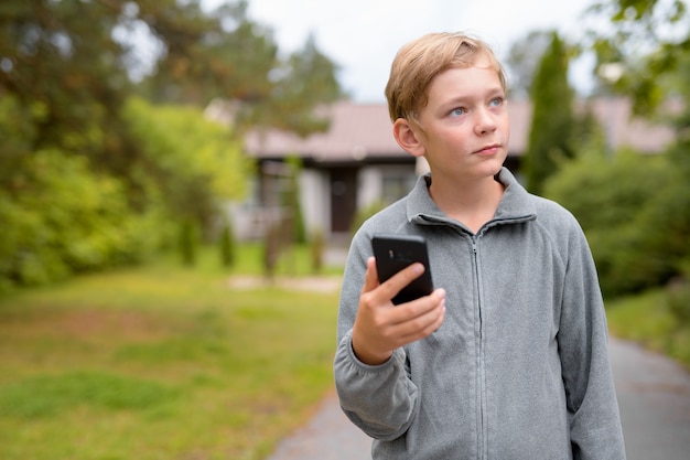 Young Blonde Handsome Boy Thinking While Using Phone At Home Out