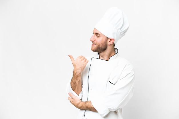 Young blonde man Chef over isolated white background pointing to the side to present a product